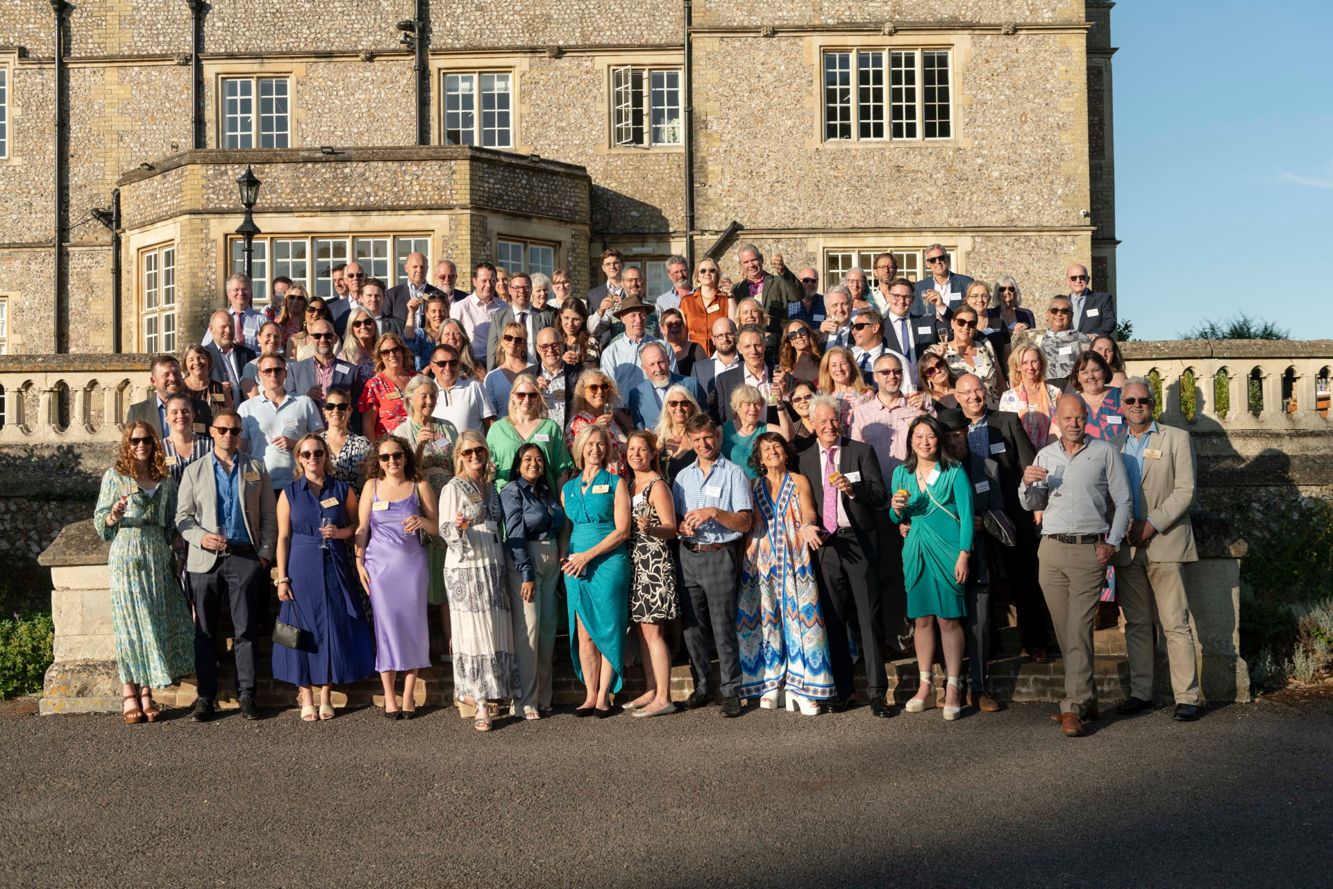 Members gathered on the steps of a country house for a group photo at the summer party