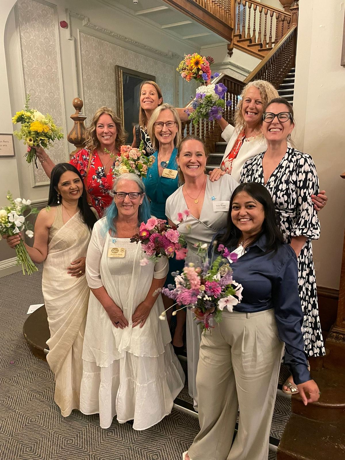 Members of Surrey Hills Enterprises gathered on a staircase with flowers at a summer celebration